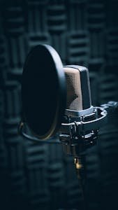 Close-up of a professional microphone with pop filter in a soundproof studio.