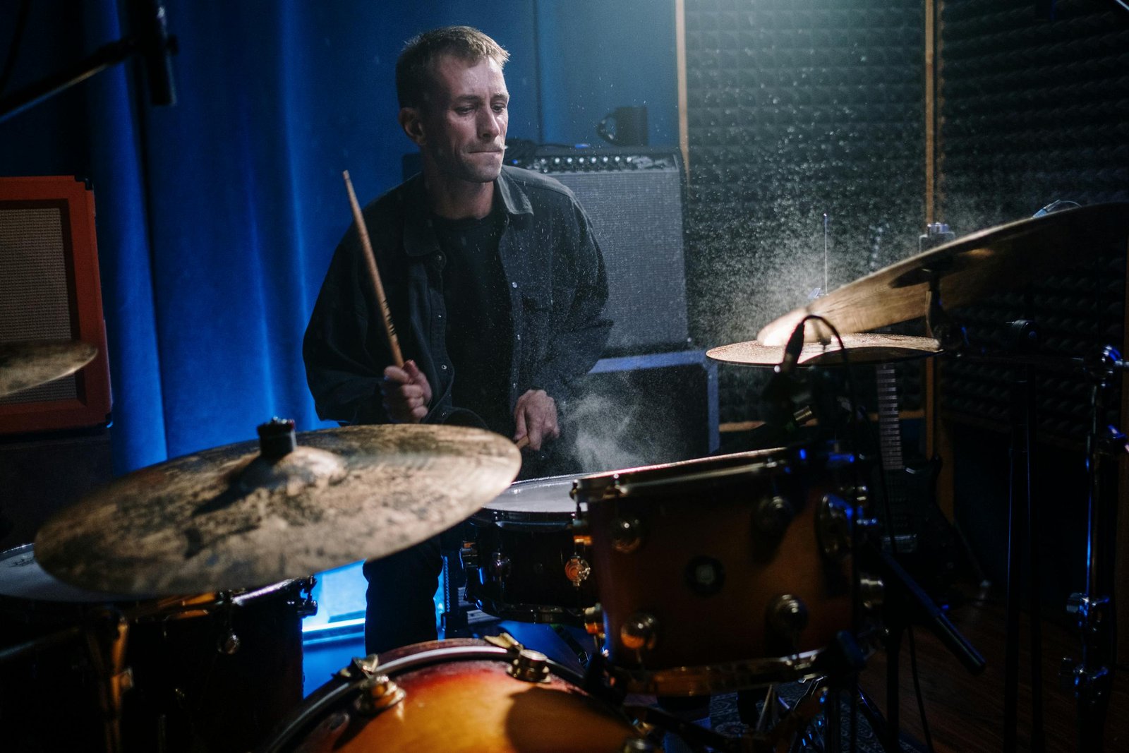 Musician playing drums with passion in a recording studio, showcasing musical performance.